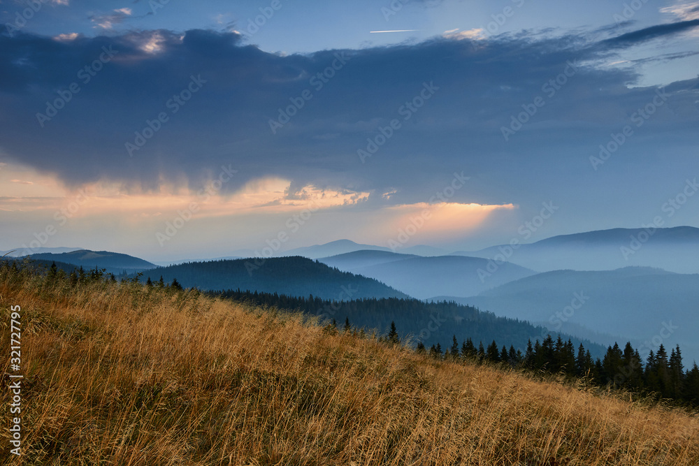 Majestic landscape of mountains at sunrise. View of the misty tops and layer hills of the mountains in the distance. Dramatic sky and rays of sunlight at morning. Concept of nature background.