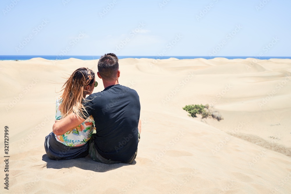 Young beautiful couple  at sitting backwards and hugging at the beach
