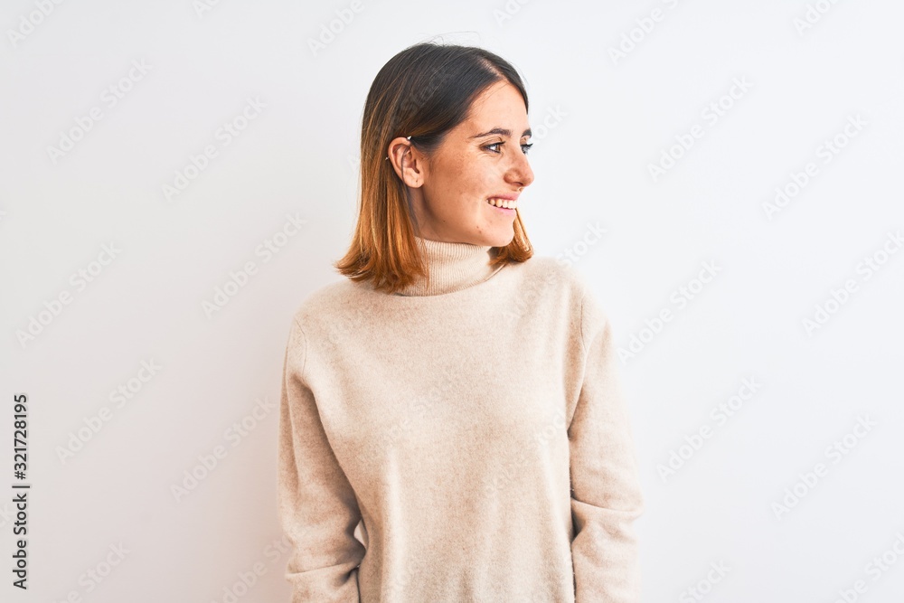 Beautiful redhead woman wearing winter turtleneck sweater over isolated background looking away to side with smile on face, natural expression. Laughing confident. Beautiful redhead woman wearing winter turtleneck sweater over isolated background looking away to side with smile on face, natural expression. Laughing confident.