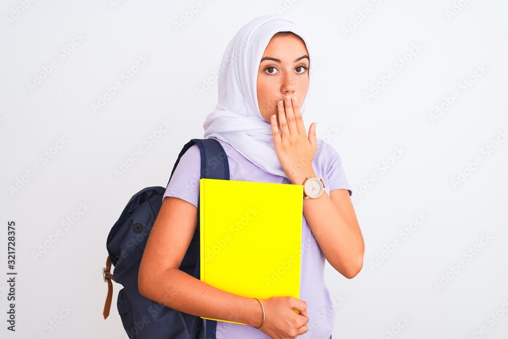 Arab student girl wearing hijab and backpack holding book over isolated white background cover mouth with hand shocked with shame for mistake, expression of fear, scared in silence, secret concept Arab student girl wearing hijab and backpack holding book over isolated white background cover mouth with hand shocked with shame for mistake, expression of fear, scared in silence, secret concept