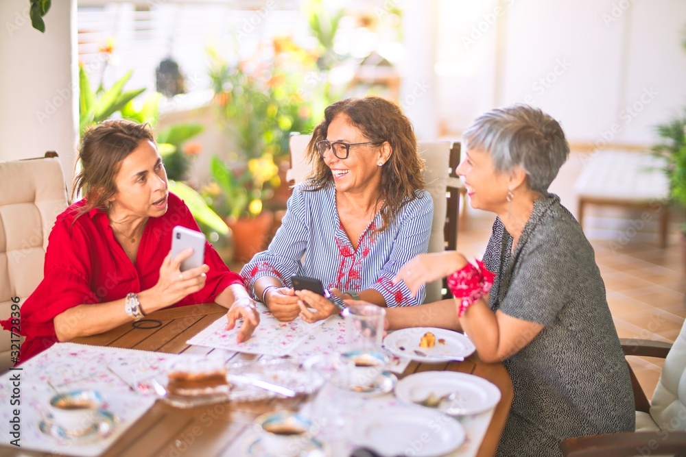 Meeting of middle age women having lunch and drinking coffee. Mature friends smiling happy using smartphone at home on a sunny day Meeting of middle age women having lunch and drinking coffee. Mature friends smiling happy using smartphone at home on a sunny day