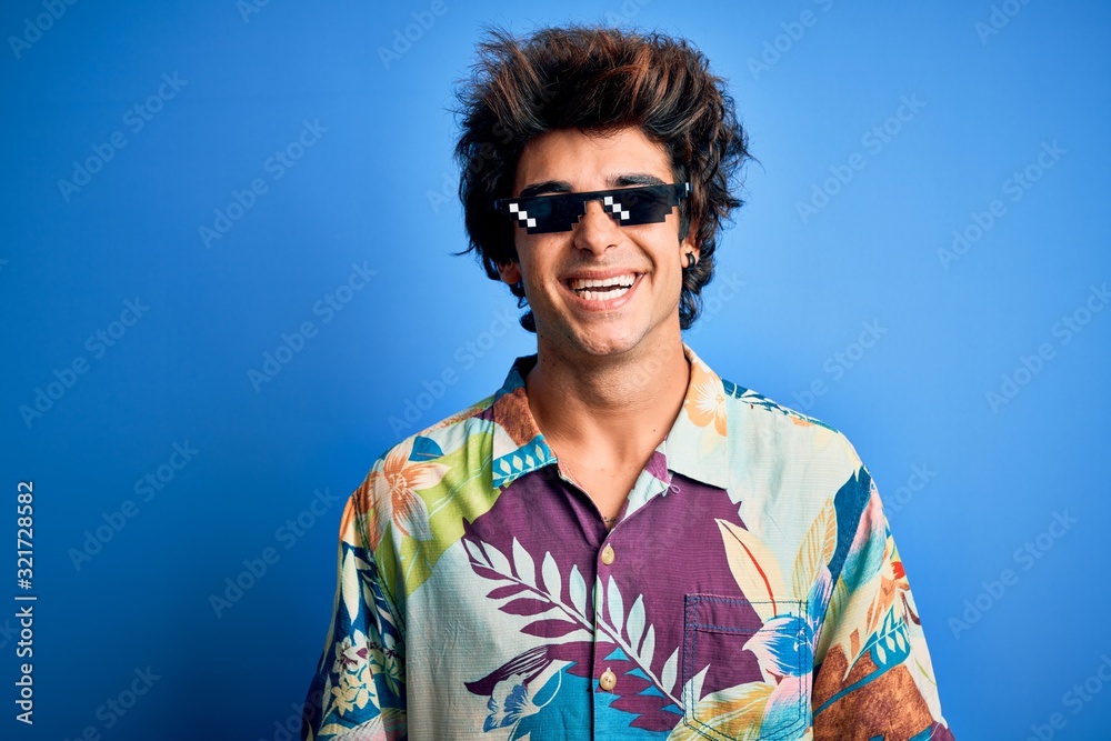 Young handsome man wearing thug life glasses standing over isolated blue background with a happy and cool smile on face. Lucky person. Young handsome man wearing thug life glasses standing over isolated blue background with a happy and cool smile on face. Lucky person.