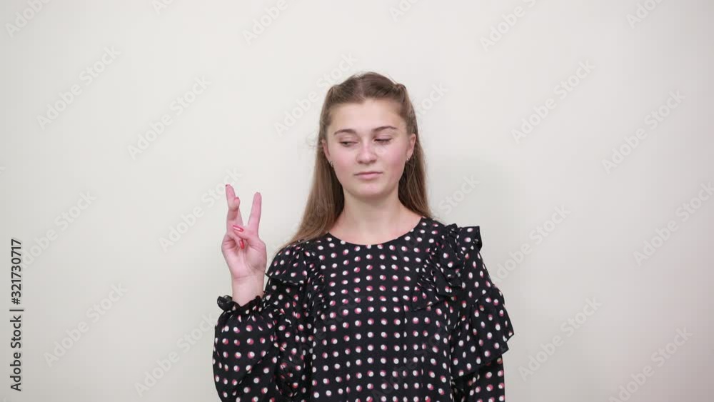 Fair-haired beautiful girl in a black dress with white circles shows three fingers of her hand and smiles