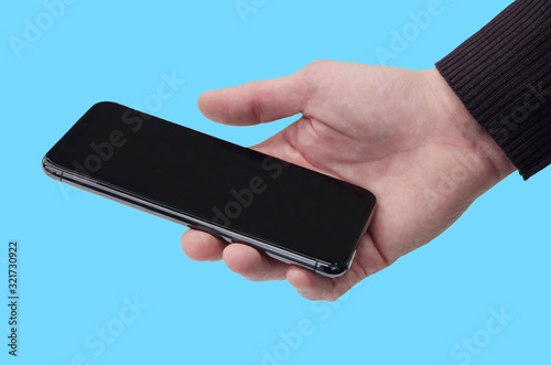 on blue background, man holds in his hand black smartphone, phone with blank screen. communication technology, modern gadgets. copy space