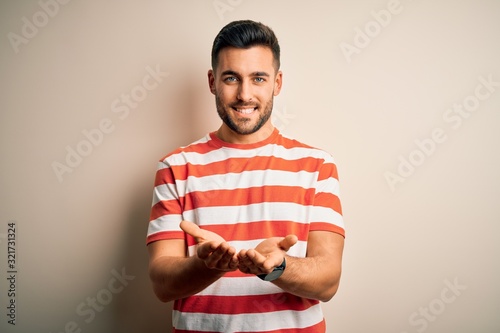 Young handsome man wearing casual striped t-shirt standing over isolated white background Smiling with hands palms together receiving or giving gesture. Hold and protection