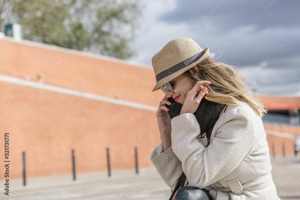 Carefree caucasian blonde girl with hat and coat speaks smiling on her mobile phone