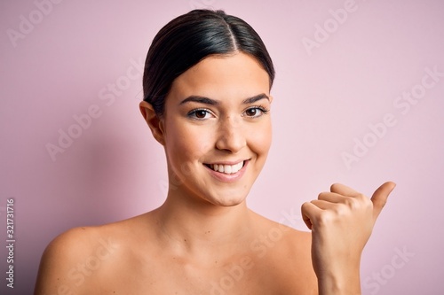 Young beautiful girl standing over isolated pink background very happy pointing with hand and finger to the side