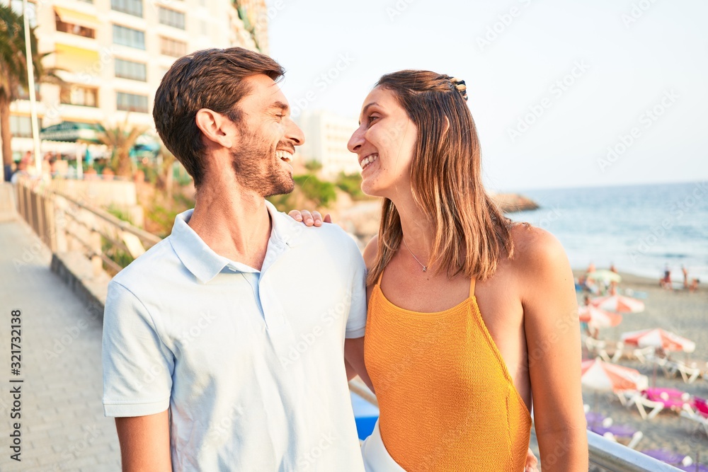 Obraz premium Young beautiful couple on vacation smiling happy and confident. Standing with smile on face hugging at the beach