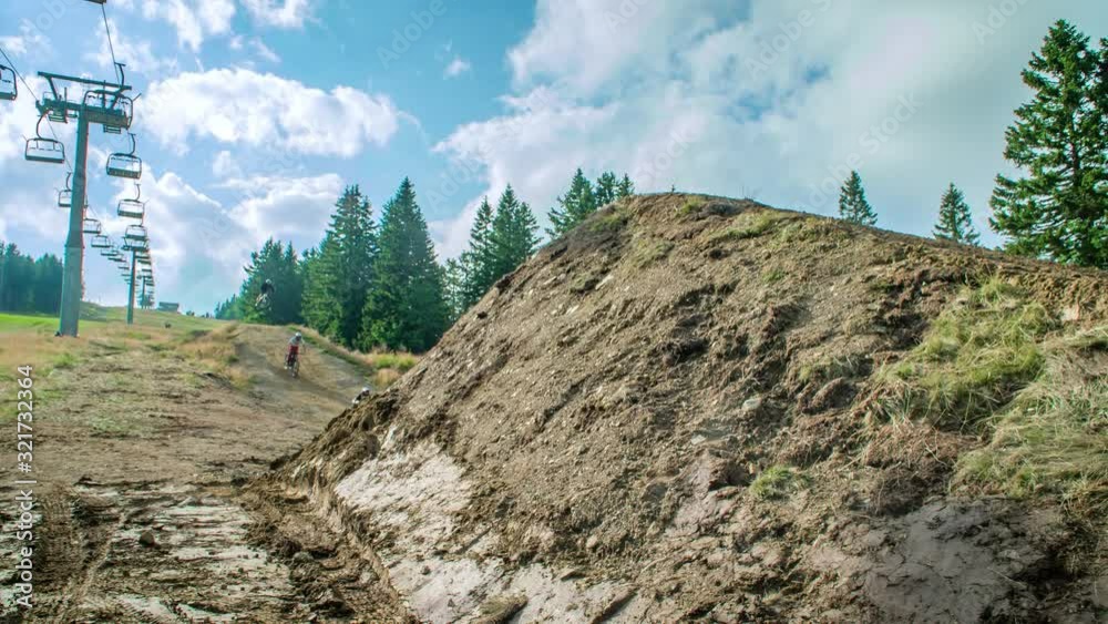 Mountain bike riders tabletop over large dirt jump in summer at ski