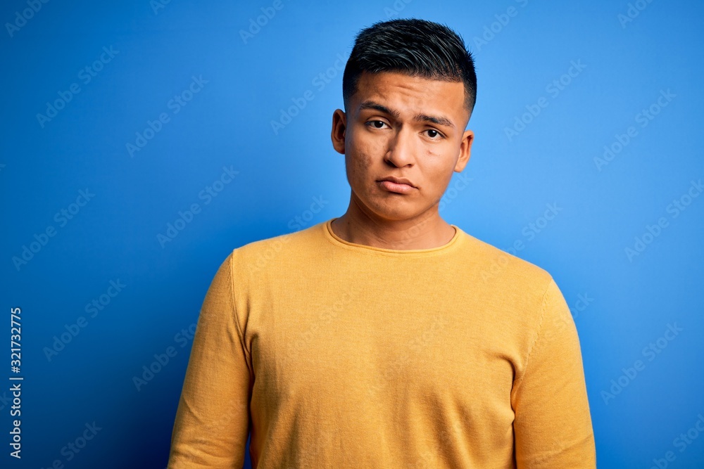 Young handsome latin man wearing yellow casual sweater over isolated blue background depressed and worry for distress, crying angry and afraid. Sad expression. Young handsome latin man wearing yellow casual sweater over isolated blue background depressed and worry for distress, crying angry and afraid. Sad expression.