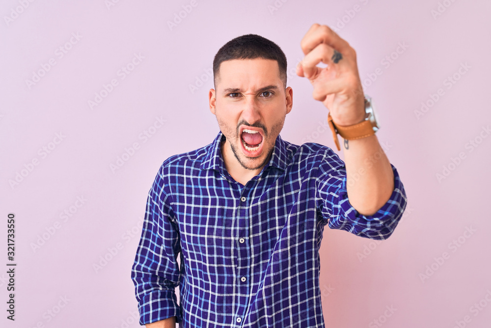 Young handsome man standing over isolated background angry and mad raising fist frustrated and furious while shouting with anger. Rage and aggressive concept. Young handsome man standing over isolated background angry and mad raising fist frustrated and furious while shouting with anger. Rage and aggressive concept.