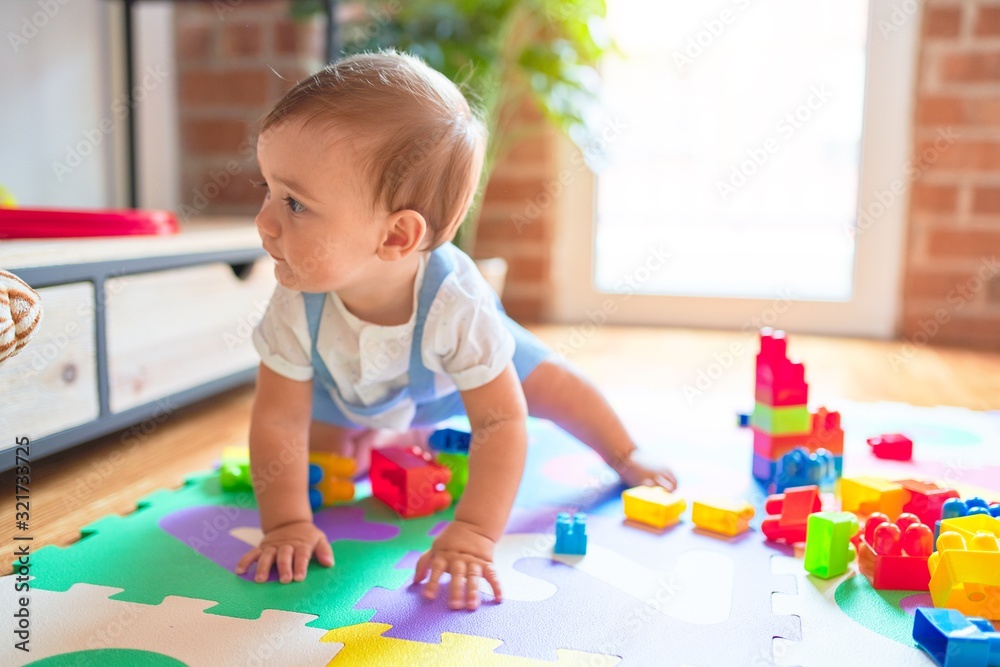 Beautiful toddler sitting on puzzle carpet playing with building blocks at kindergarten Beautiful toddler sitting on puzzle carpet playing with building blocks at kindergarten