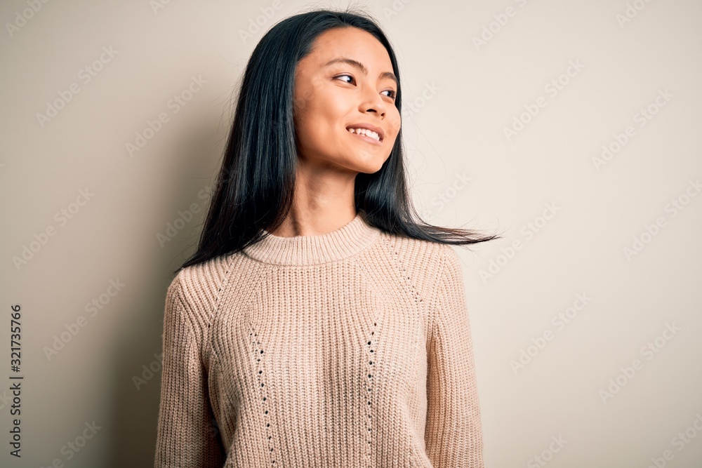 Young beautiful chinese woman wearing casual sweater over isolated white background looking away to side with smile on face, natural expression. Laughing confident. Young beautiful chinese woman wearing casual sweater over isolated white background looking away to side with smile on face, natural expression. Laughing confident.