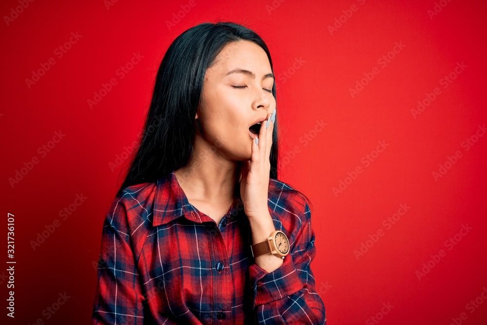 Young beautiful chinese woman wearing casual shirt over isolated red background bored yawning tired covering mouth with hand. Restless and sleepiness. Young beautiful chinese woman wearing casual shirt over isolated red background bored yawning tired covering mouth with hand. Restless and sleepiness.