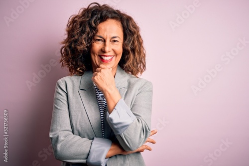 Middle age beautiful businesswoman wearing elegant jacket over isolated pink background looking confident at the camera smiling with crossed arms and hand raised on chin. Thinking positive. photo