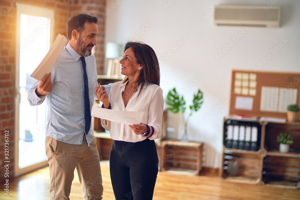 Two middle age business workers smiling happy and confident. Standing with smile on face working together holding documents at the office Two middle age business workers smiling happy and confident. Standing with smile on face working together holding documents at the office
