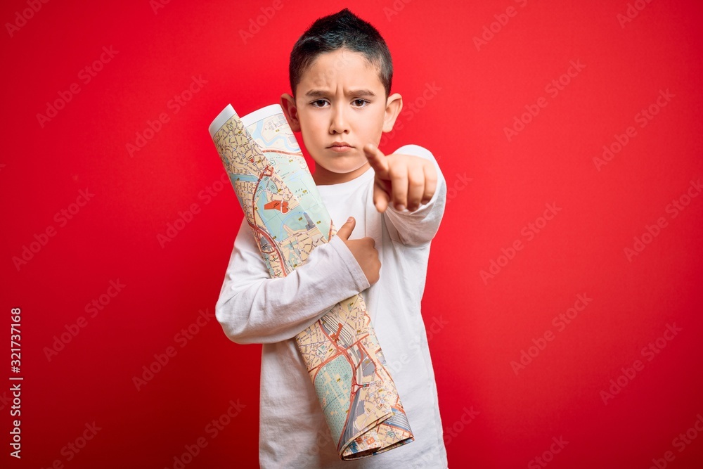 Young little boy kid looking at turist city destination map over red isolated background pointing with finger to the camera and to you, hand sign, positive and confident gesture from the front Young little boy kid looking at turist city destination map over red isolated background pointing with finger to the camera and to you, hand sign, positive and confident gesture from the front