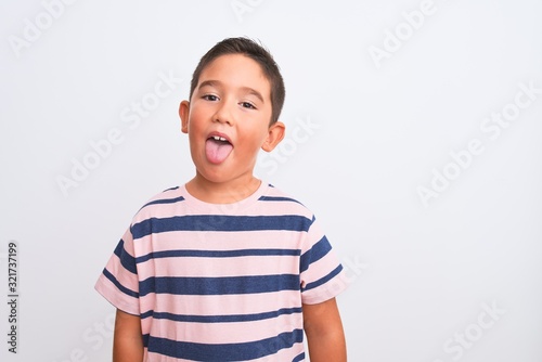 Beautiful kid boy wearing casual striped t-shirt standing over isolated white background sticking tongue out happy with funny expression. Emotion concept.