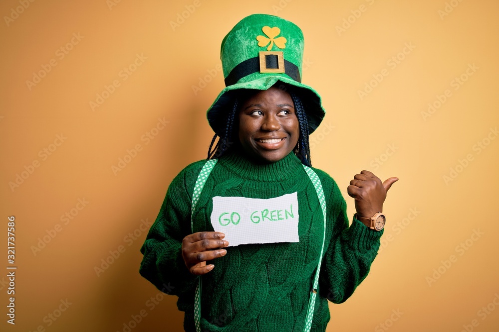 Plus size african american woman wearing green hat holding paper on saint patricks day pointing and showing with thumb up to the side with happy face smiling Plus size african american woman wearing green hat holding paper on saint patricks day pointing and showing with thumb up to the side with happy face smiling