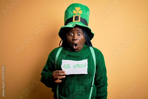 Plus size african american woman wearing green hat holding paper on saint patricks day scared in shock with a surprise face, afraid and excited with fear expression