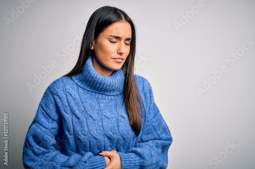 Young beautiful brunette woman wearing casual turtleneck sweater over white background with hand on stomach because indigestion, painful illness feeling unwell. Ache concept. © Krakenimages.com