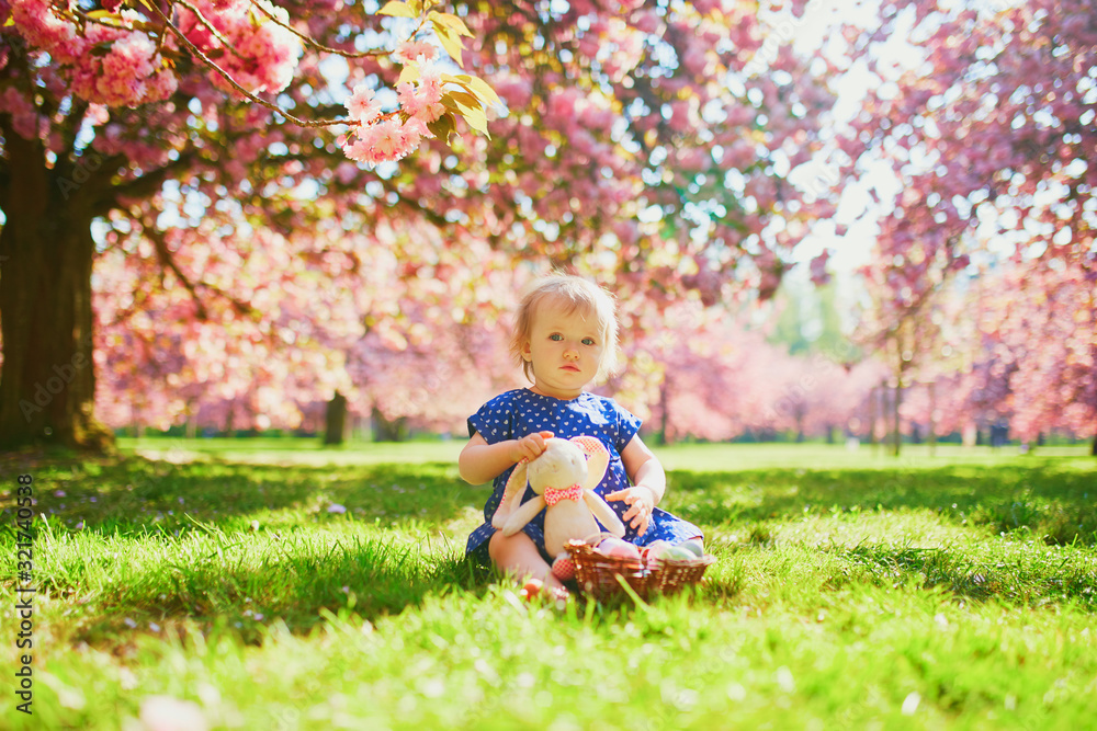 Cute one year old girl sitting on the grass and eating strawberries Cute one year old girl sitting on the grass and eating strawberries