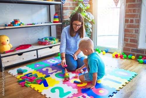 Young caucasian child playing at playschool with teacher. Mother and son playing with wooden pieces train at playroom photo