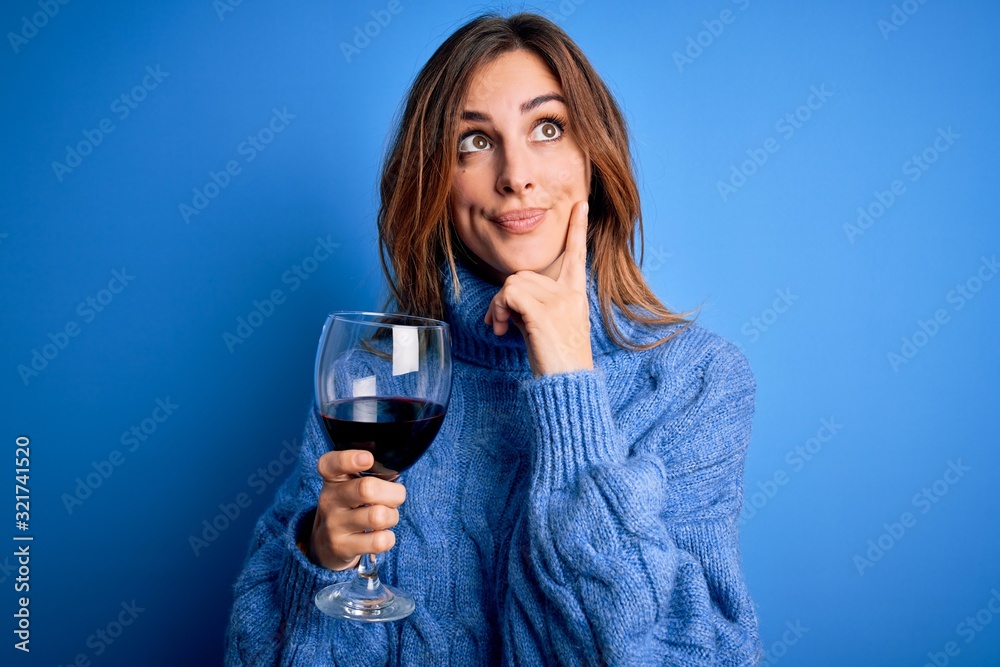 Young beautiful brunette woman drinking glass of red wine over isolated blue background serious face thinking about question, very confused idea Young beautiful brunette woman drinking glass of red wine over isolated blue background serious face thinking about question, very confused idea