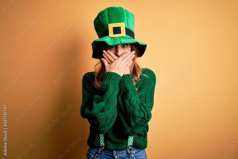 Beautiful brunette woman wearing green hat with clover celebrating saint patricks day shocked covering mouth with hands for mistake. Secret concept. Beautiful brunette woman wearing green hat with clover celebrating saint patricks day shocked covering mouth with hands for mistake. Secret concept.