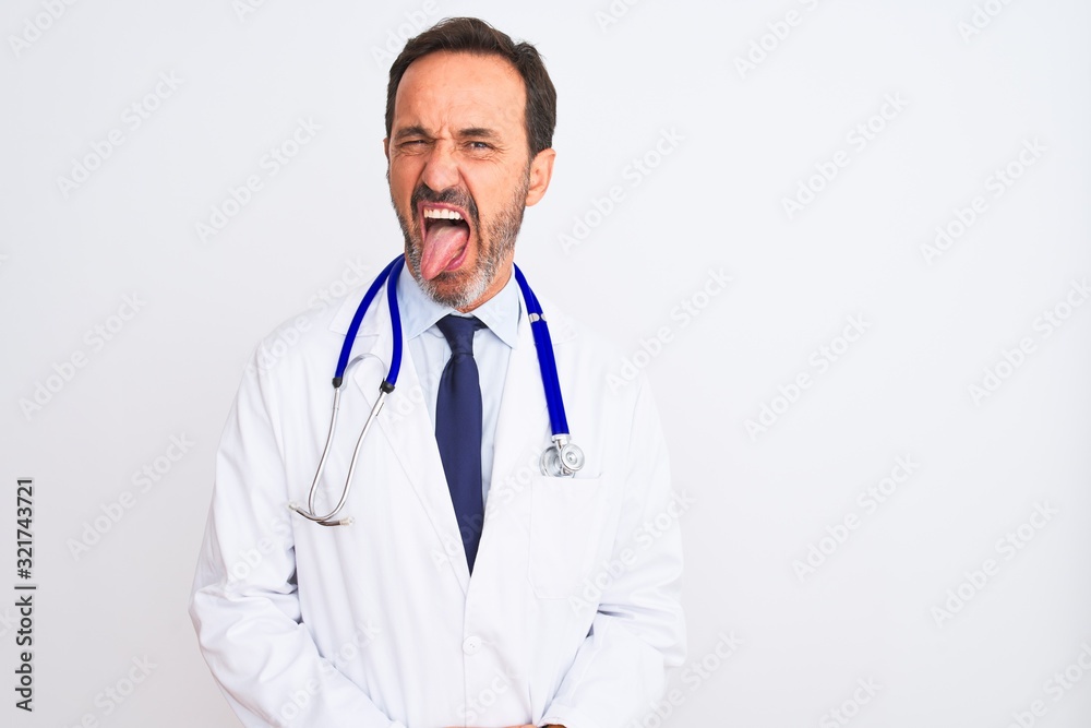 Middle age doctor man wearing coat and stethoscope standing over isolated white background sticking tongue out happy with funny expression. Emotion concept.