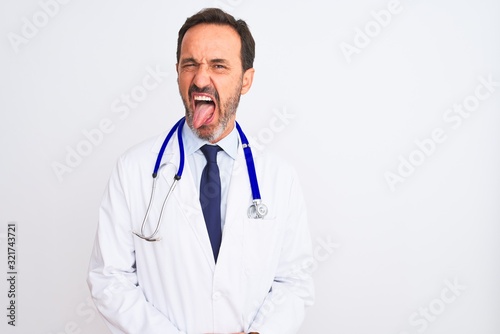 Middle age doctor man wearing coat and stethoscope standing over isolated white background sticking tongue out happy with funny expression. Emotion concept.