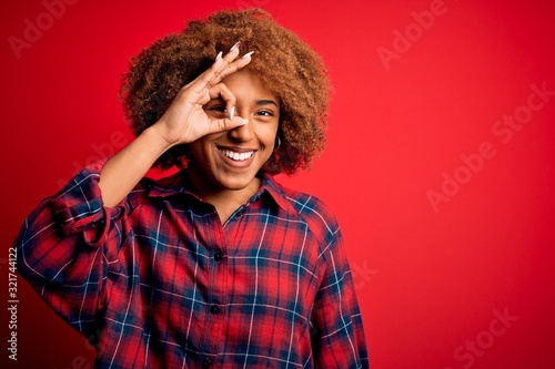 Young beautiful African American afro woman with curly hair wearing casual shirt doing ok gesture with hand smiling, eye looking through fingers with happy face. © Krakenimages.com