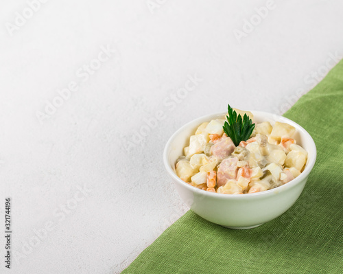 Traditional Russian Olivier Salad with chicken, eggs, potatoes, pickles, green peas, carrots and parsley in a Cup on a light background