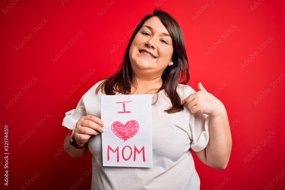 Beautiful brunette plus size woman holding love mom message celebrating mothers day with surprise face pointing finger to himself Beautiful brunette plus size woman holding love mom message celebrating mothers day with surprise face pointing finger to himself