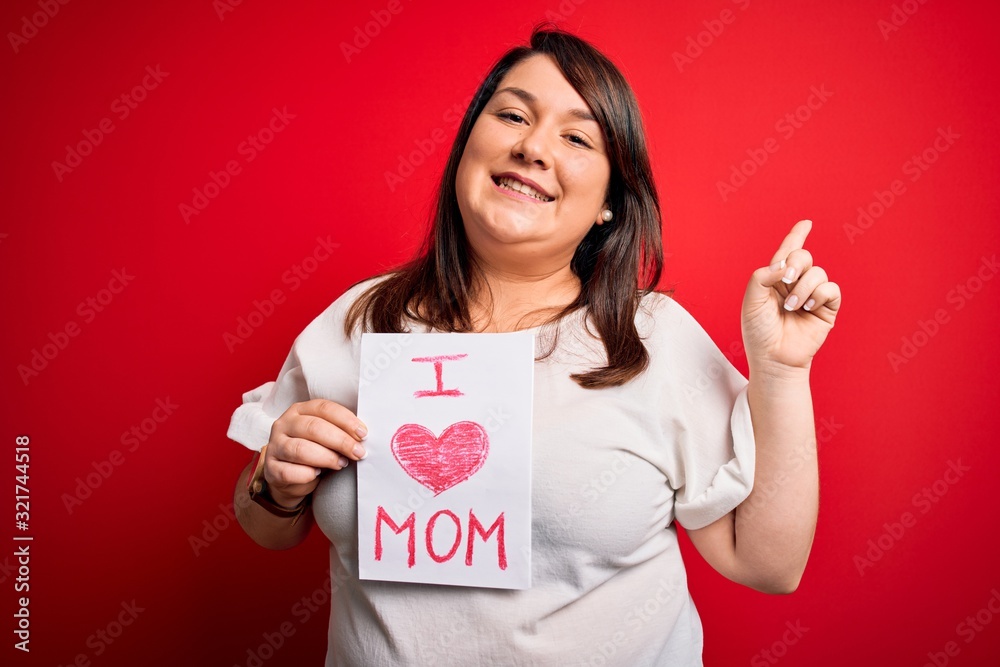 Beautiful brunette plus size woman holding love mom message celebrating mothers day very happy pointing with hand and finger to the side Beautiful brunette plus size woman holding love mom message celebrating mothers day very happy pointing with hand and finger to the side