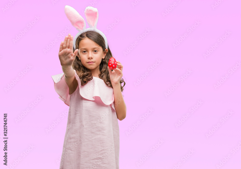 Brunette hispanic girl wearing easter rabbit ears with open hand doing stop sign with serious and confident expression, defense gesture