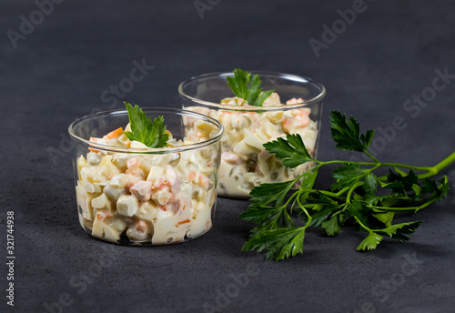 Traditional Russian salad olivier with chicken, eggs, potatoes, pickles, green peas, carrots and parsley in a Cup on a dark background