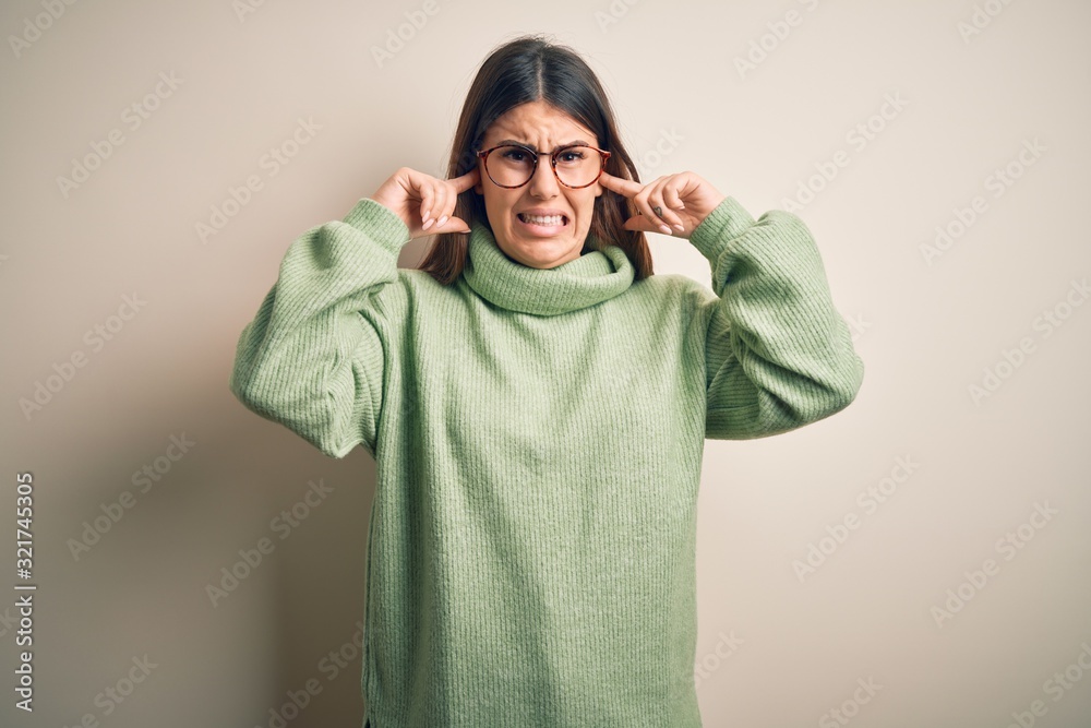 Young beautiful woman wearing casual sweater standing over isolated white background covering ears with fingers with annoyed expression for the noise of loud music. Deaf concept. Young beautiful woman wearing casual sweater standing over isolated white background covering ears with fingers with annoyed expression for the noise of loud music. Deaf concept.