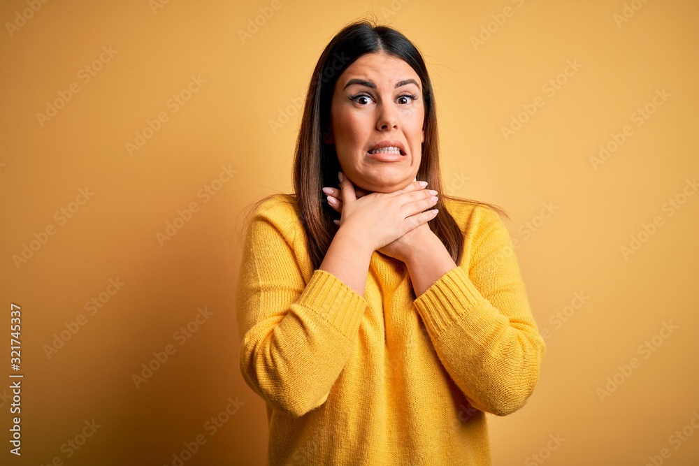 Young beautiful woman wearing casual sweater over yellow isolated background shouting and suffocate because painful strangle. Health problem. Asphyxiate and suicide concept. Young beautiful woman wearing casual sweater over yellow isolated background shouting and suffocate because painful strangle. Health problem. Asphyxiate and suicide concept.