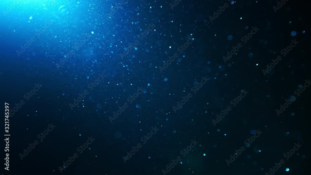 Blue glitter background. Underwater particles flying and shining in spotlight, shot with depth of field. Space dust beautiful bokeh abstract background