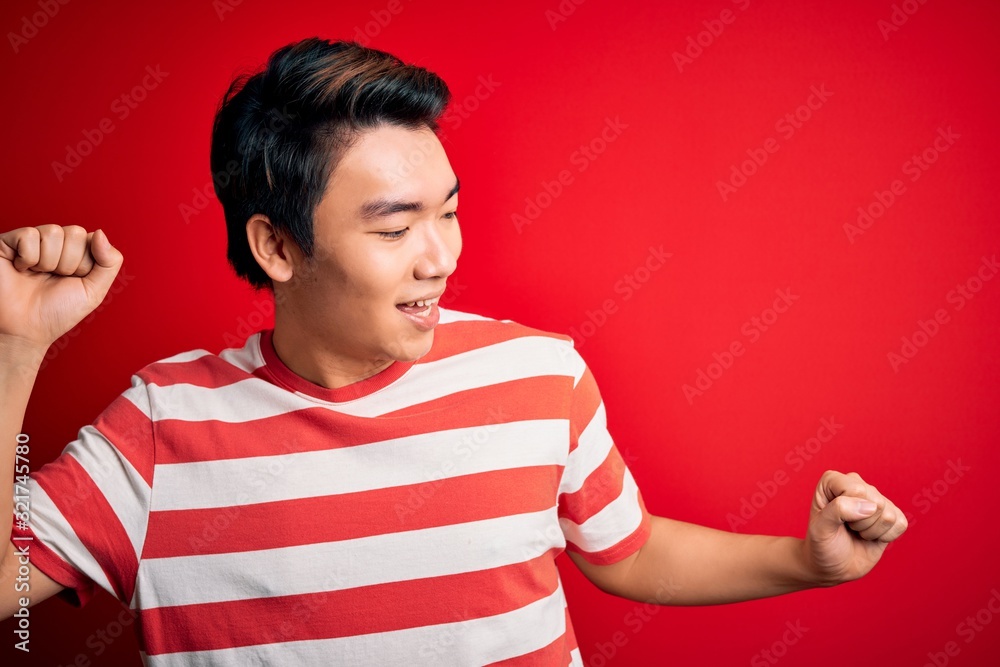 Young handsome chinese man wearing casual striped t-shirt standing over red background Dancing happy and cheerful, smiling moving casual and confident listening to music Young handsome chinese man wearing casual striped t-shirt standing over red background Dancing happy and cheerful, smiling moving casual and confident listening to music