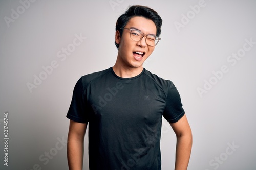 Young handsome chinese man wearing black t-shirt and glasses over white background winking looking at the camera with sexy expression, cheerful and happy face.