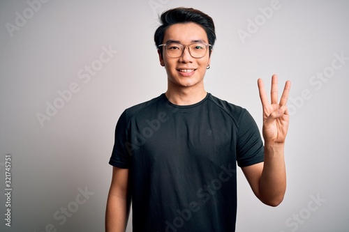 Young handsome chinese man wearing black t-shirt and glasses over white background showing and pointing up with fingers number three while smiling confident and happy. © Krakenimages.com
