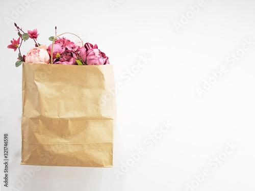 Paper shopping bag with flower in it presented on white background. Ecology concept. Peonies in a brown kraft bag. Spring sale, shop, greeting card. Copy space. Floral gift idea. Springtime holiday.