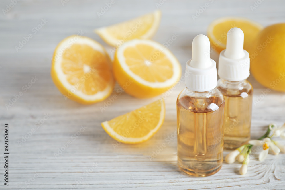 Bottles of citrus essential oil, flower and lemons on white wooden table. Space for text