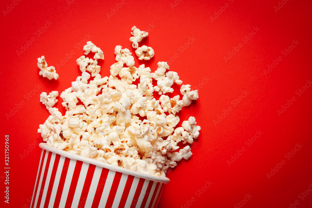 Overturned paper cup with delicious popcorn on red background, top view Overturned paper cup with delicious popcorn on red background, top view