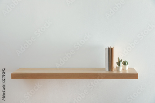Vászonkép Wooden shelf with books and decorative cactuses on light wall