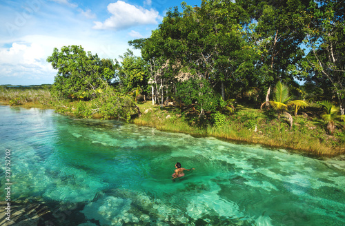 Fototapeta Naklejka Na Ścianę i Meble -  Man in rapids at seven colored lagoon surrounded by tropical plants in Bacalar, Quintana Roo, Mexico