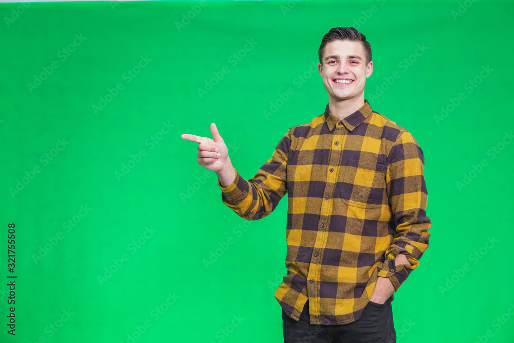 Portrait of attractive happy guy weared in checkered shirt, looking at the camera, turning your attention to copy space on green backhround, where should be something important. Portrait of attractive happy guy weared in checkered shirt, looking at the camera, turning your attention to copy space on green backhround, where should be something important.