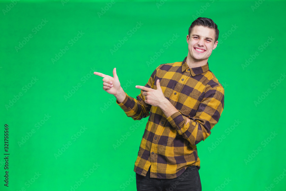 Portrait of attractive happy guy weared in checkered shirt, looking at the camera, turning your attention to copy space on green backhround, where should be something important. Portrait of attractive happy guy weared in checkered shirt, looking at the camera, turning your attention to copy space on green backhround, where should be something important.